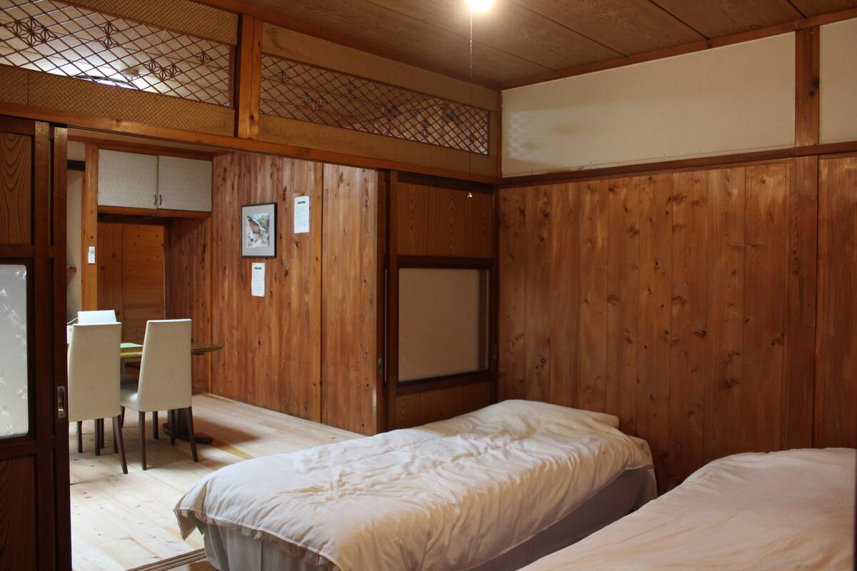 Ein Zimmer mit Holzwandverkleidung, einem Bett, einem Schreibtisch mit Stühlen und einem kleinen Fenster.