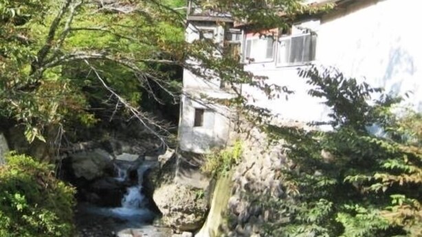 A building with a red roof, a stone wall, and a small waterfall. - Taikengata Kominka Minshuku Kajika Club (Nanmoku)