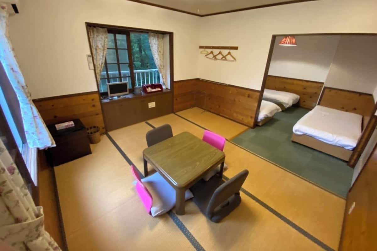 Ein Zimmer mit Etagenbett, kleinem Tisch mit Stühlen, einem Fenster mit Vorhängen und einem an der Wand befestigten Fernseher.