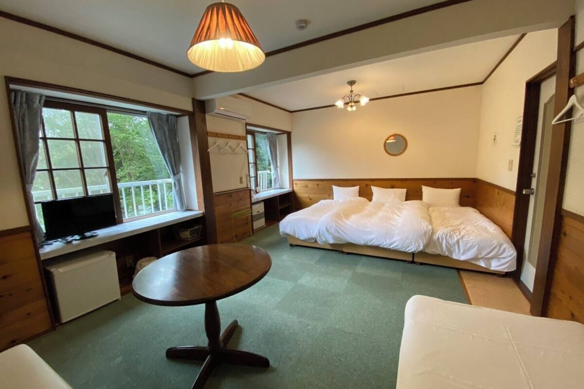 Ein Schlafzimmer mit einem Bett, einem runden Tisch, einem Fernseher und einem Fenster mit Blick auf Grünflächen.