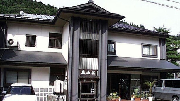 A two-story building with a central entrance, a vehicle parked in front, and a sign with Japanese characters. - Ryokan Keizanso (Nasushiobara)