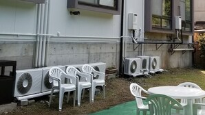 A building with multiple windows, outdoor air conditioning units, and a green outdoor area with white plastic chairs and tables. - Ryokan Keizanso (Nasushiobara)