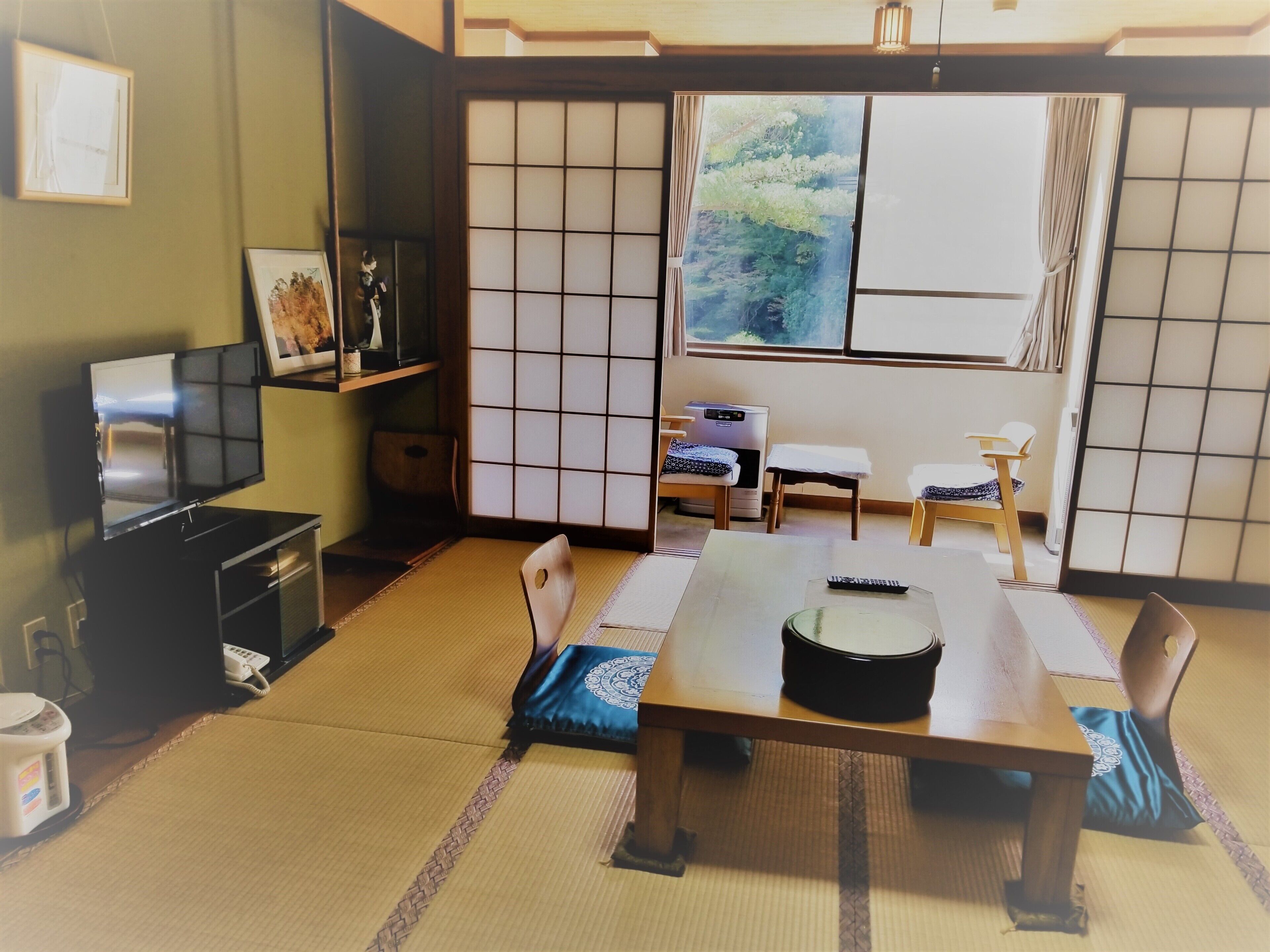 A traditional Japanese room with tatami flooring, a low table with a black tray, a television, and a window with a view of greenery.