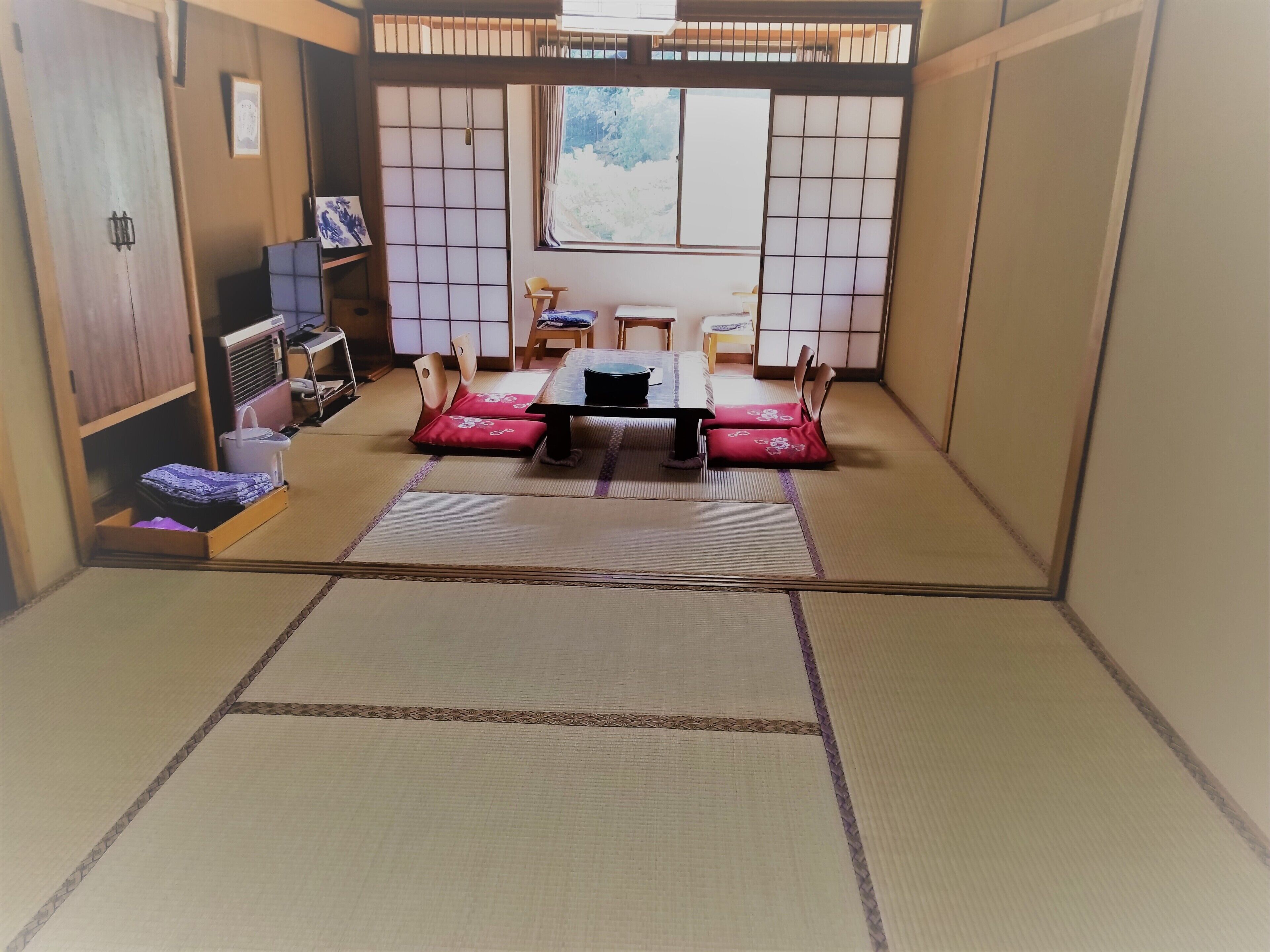 A tatami mat room with a low table, chairs, and a futon bed.