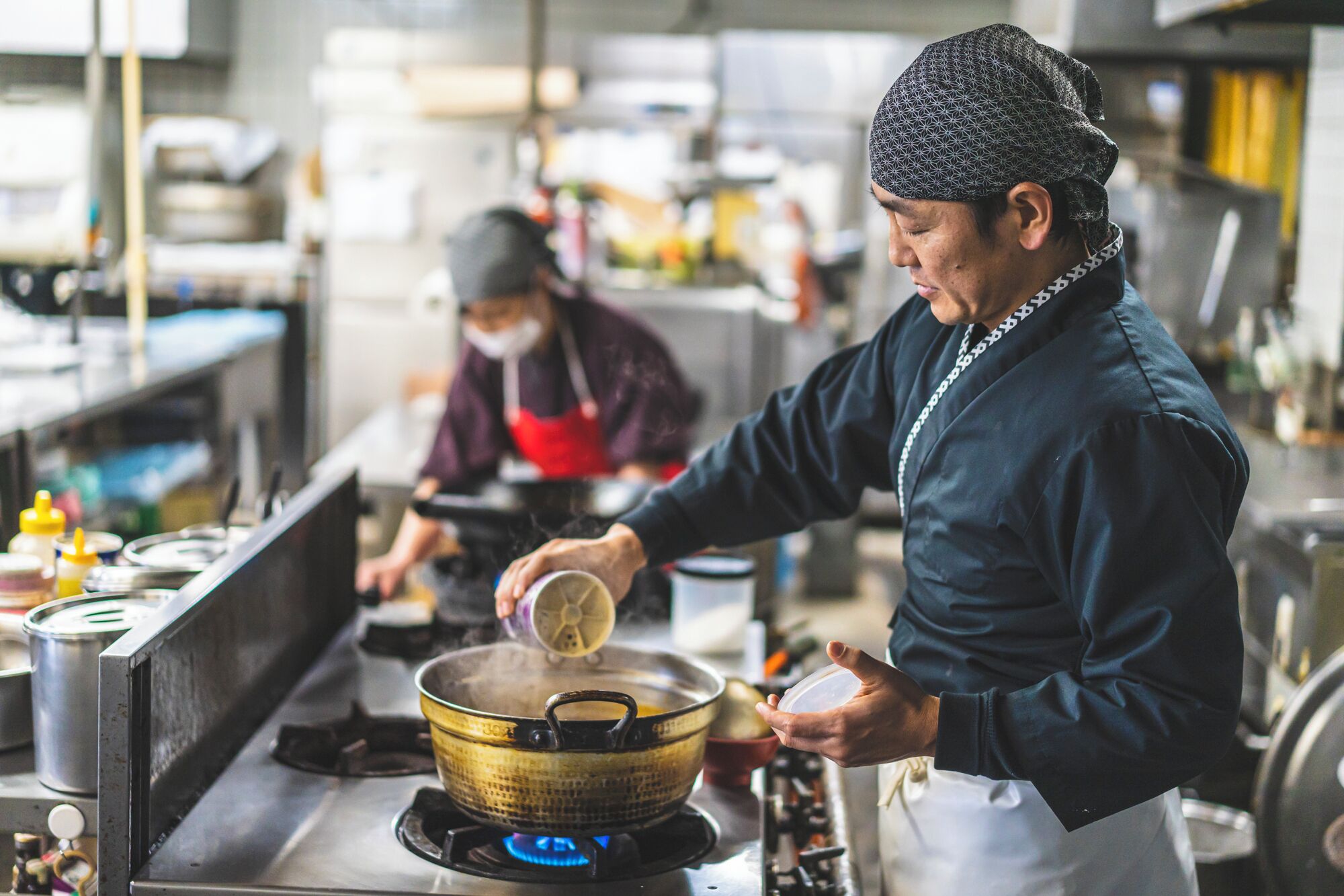 Una persona cocinando en una cocina con electrodomésticos de acero inoxidable y una olla sobre una estufa a gas.