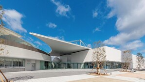 Een modern gebouw met een gebogen glazen gevel, een opvallende uitkragende constructie en een kaartverkoopkantoor.