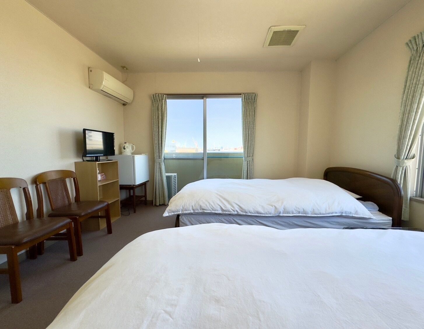 A hotel room with a bed, a desk with a TV, a chair, and a window with curtains.