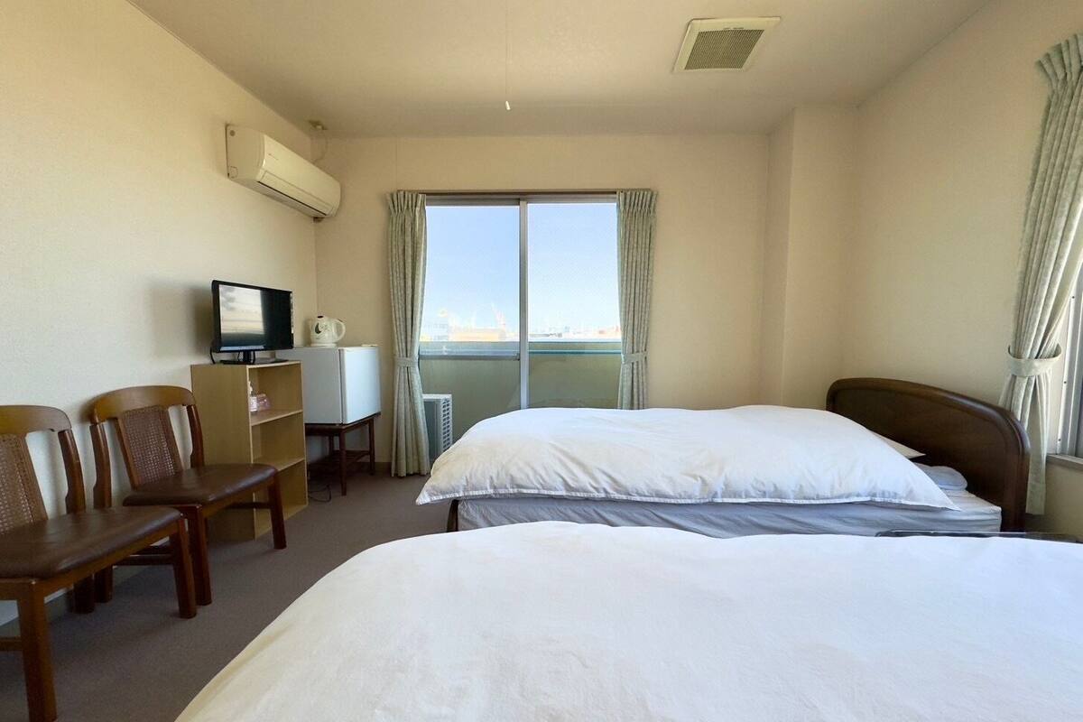 A hotel room with a bed, a desk with a TV, a chair, and a window with curtains.