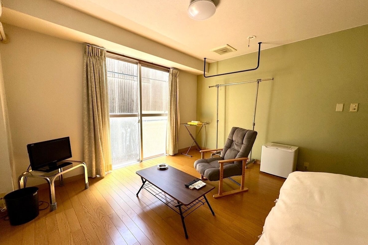 A hotel room with a television, a desk, a chair, a bed, and a window with curtains.