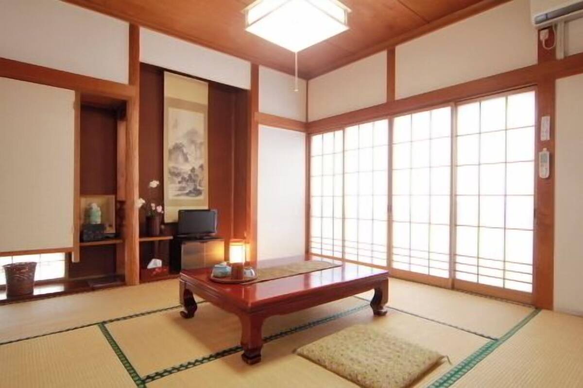 Une pièce de style japonais traditionnel, avec un sol recouvert de tatamis, une basse table en bois, un téléviseur et des portes coulissantes.