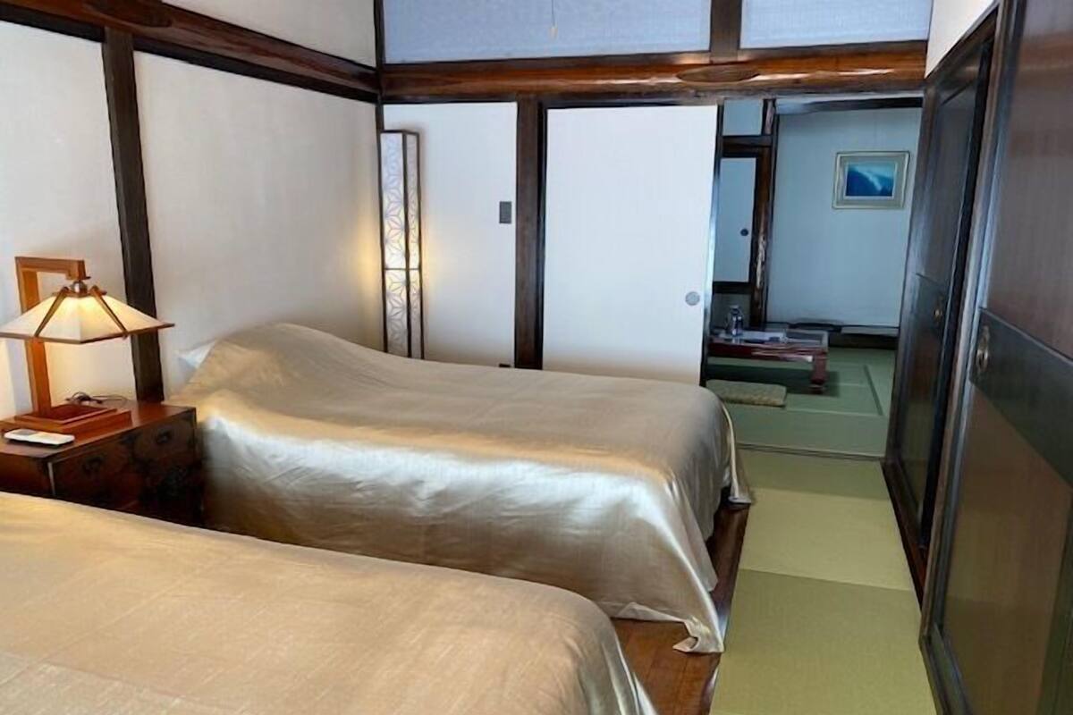 Une chambre avec deux lits, une table de chevet avec une lampe et une porte coulissante donnant sur une autre pièce.