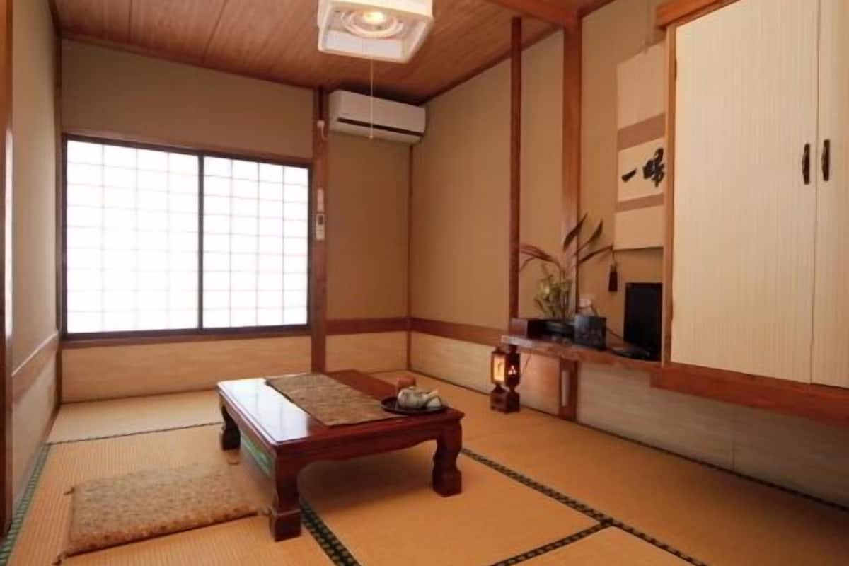 Une pièce de style japonais traditionnel, avec un sol recouvert de tatamis, une petite table en bois, une porte coulissante et un ventilateur de plafond.