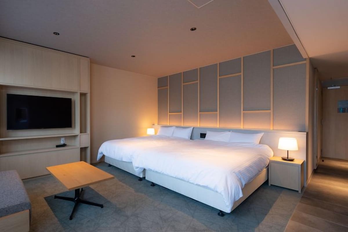 A modern hotel room with a large bed, a TV mounted on the wall, a small table, and a sofa.