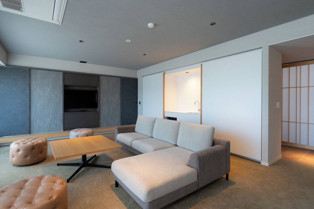 Un salon moderne avec un canapé d’angle, des poufs, une table basse et un téléviseur.
