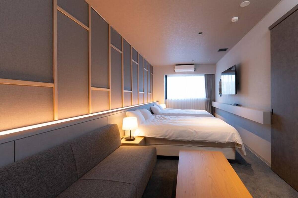 Une chambre d’hôtel avec deux lits, un canapé, une table en bois et un téléviseur fixé au mur.