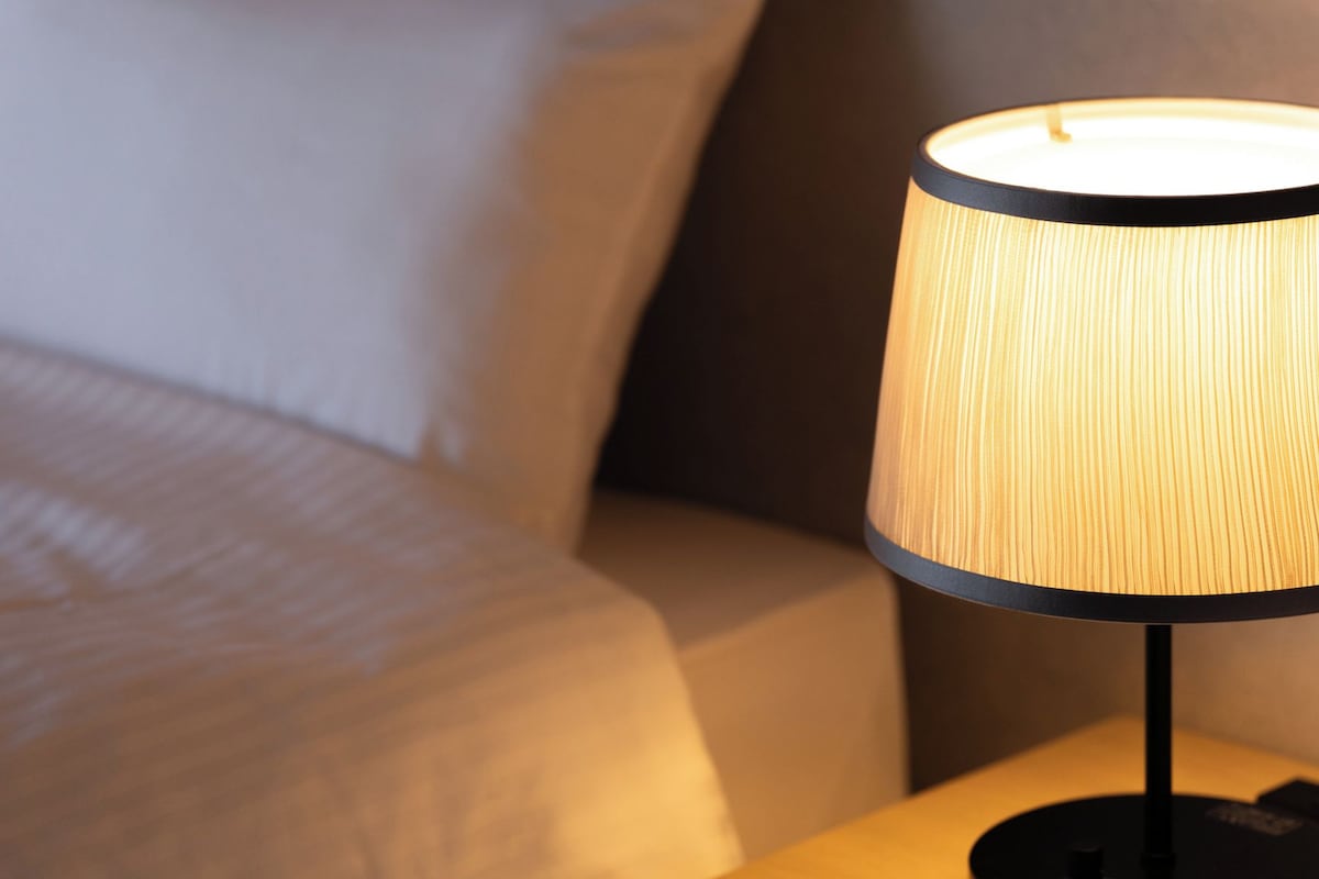 A bed with white bedding and a nightstand with a lamp.