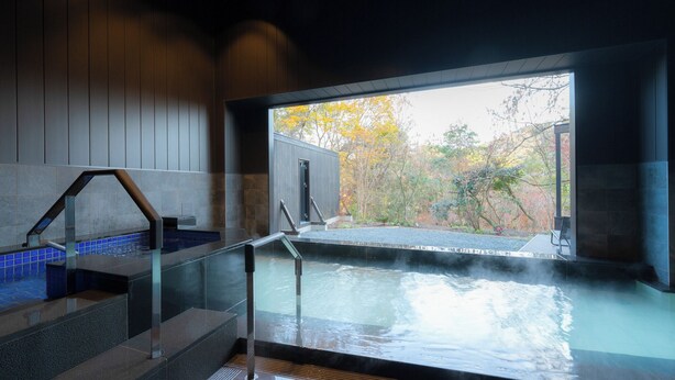 A modern indoor pool with clear glass walls, a wooden interior, and a view of autumn foliage. - OND Hotel (Takeo)