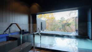 Una piscina interna moderna con pareti in vetro trasparente, interni in legno e vista sul fogliame autunnale.
