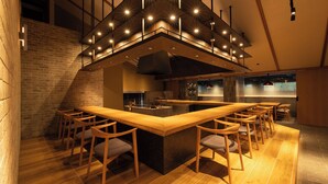 A bar area with a long counter, multiple stools, and a modern ceiling light fixture. - OND Hotel (Takeo)