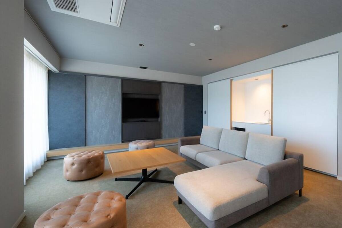 Un salon moderne avec un canapé d’angle, des poufs, une table basse et un téléviseur.