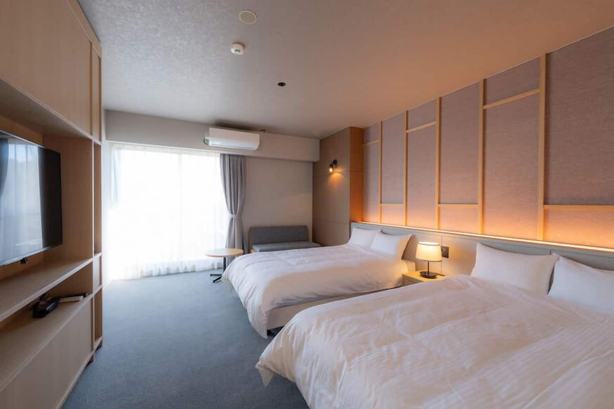 Une chambre d’hôtel avec deux lits, une télévision, un bureau et une fenêtre avec des rideaux.
