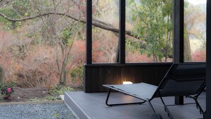 A modern outdoor seating area with a view of trees and a fireplace. - OND Hotel (Takeo)