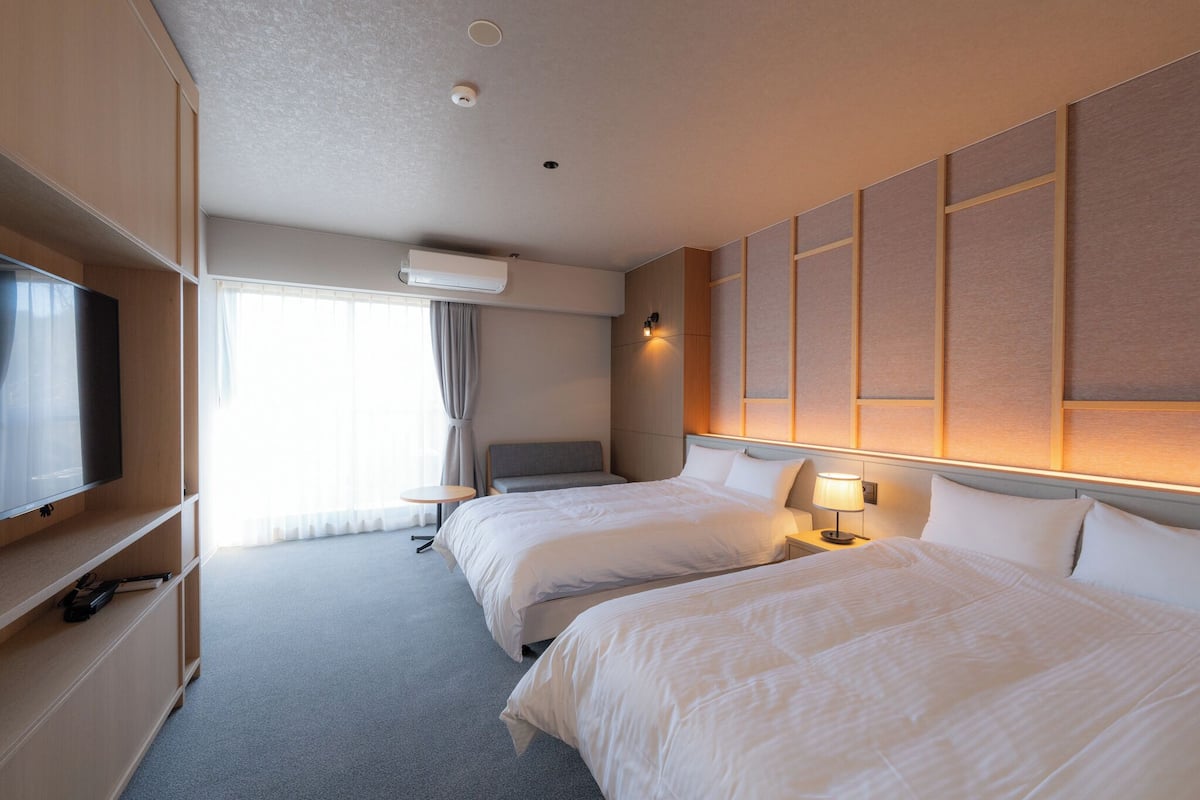 Une chambre d’hôtel avec deux lits, une télévision, un bureau et une fenêtre avec des rideaux.