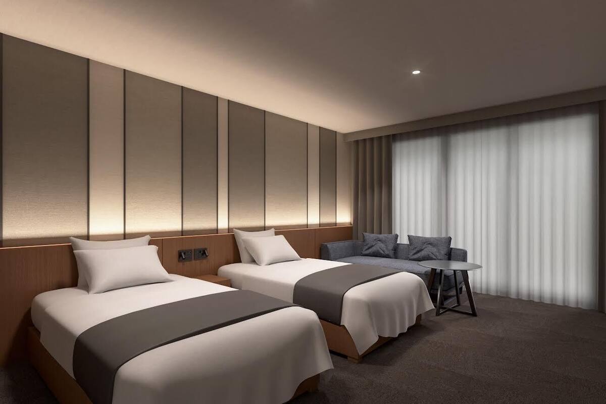 Une chambre d’hôtel avec deux lits, une petite table et une grande fenêtre avec des rideaux.