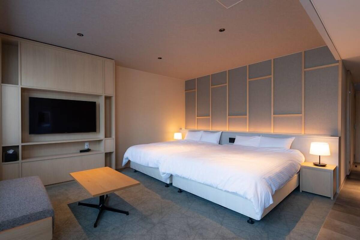 Une chambre d’hôtel moderne avec un grand lit, un téléviseur fixé au mur, une petite table et un canapé.