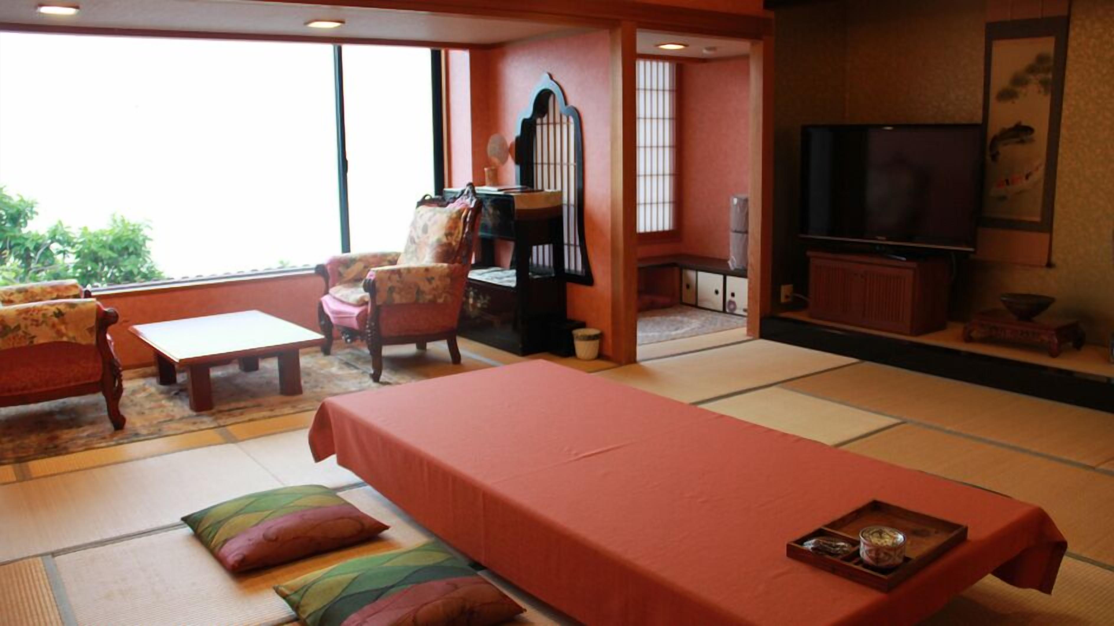 A traditional Japanese-style room with tatami flooring, a low table, a sofa, a chair, a television, and a sliding door leading to another room.
