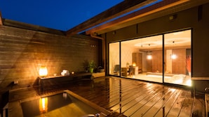 A modern hotel room with a wooden deck, a hot tub, and a sliding glass door leading to a bedroom with a large bed and a bathroom. - Tara Takezaki Onsen Kaijyoukan (Tara)
