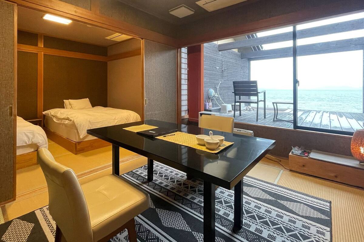 A hotel room with a bed, a desk, a chair, a table, and a view of the sea.