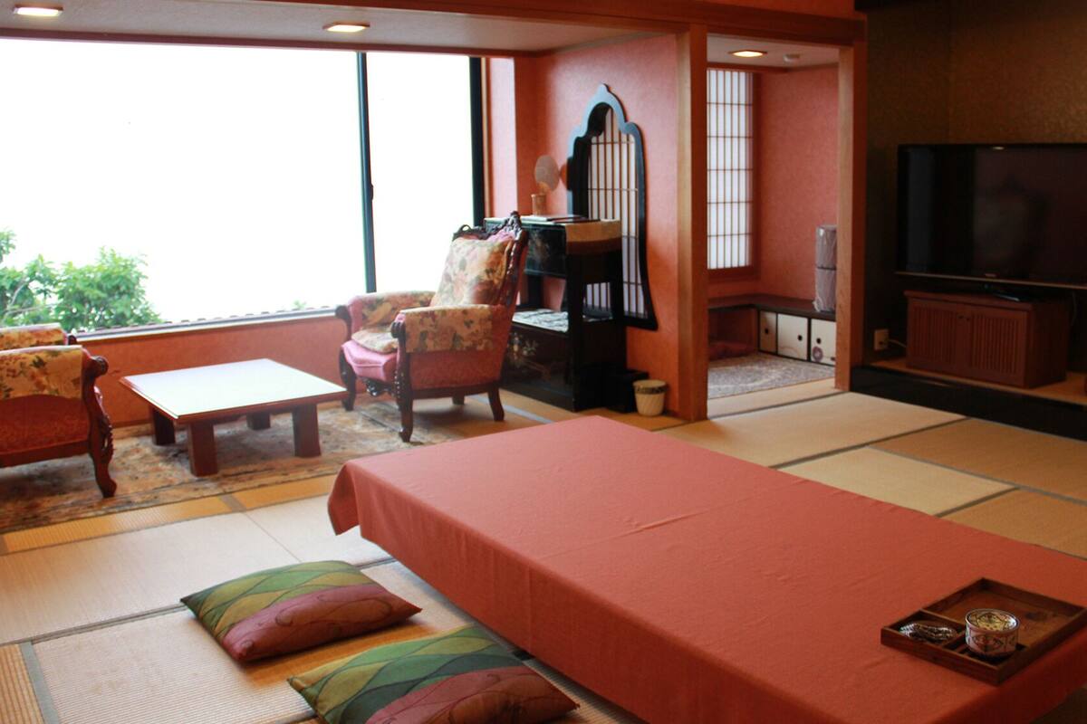A traditional Japanese-style living room with tatami flooring, a low table, a sofa, a chair, and a television.