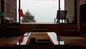 A room with a view of the sea, a wooden table, a red chair, and a bench. - Tara Takezaki Onsen Kaijyoukan (Tara)