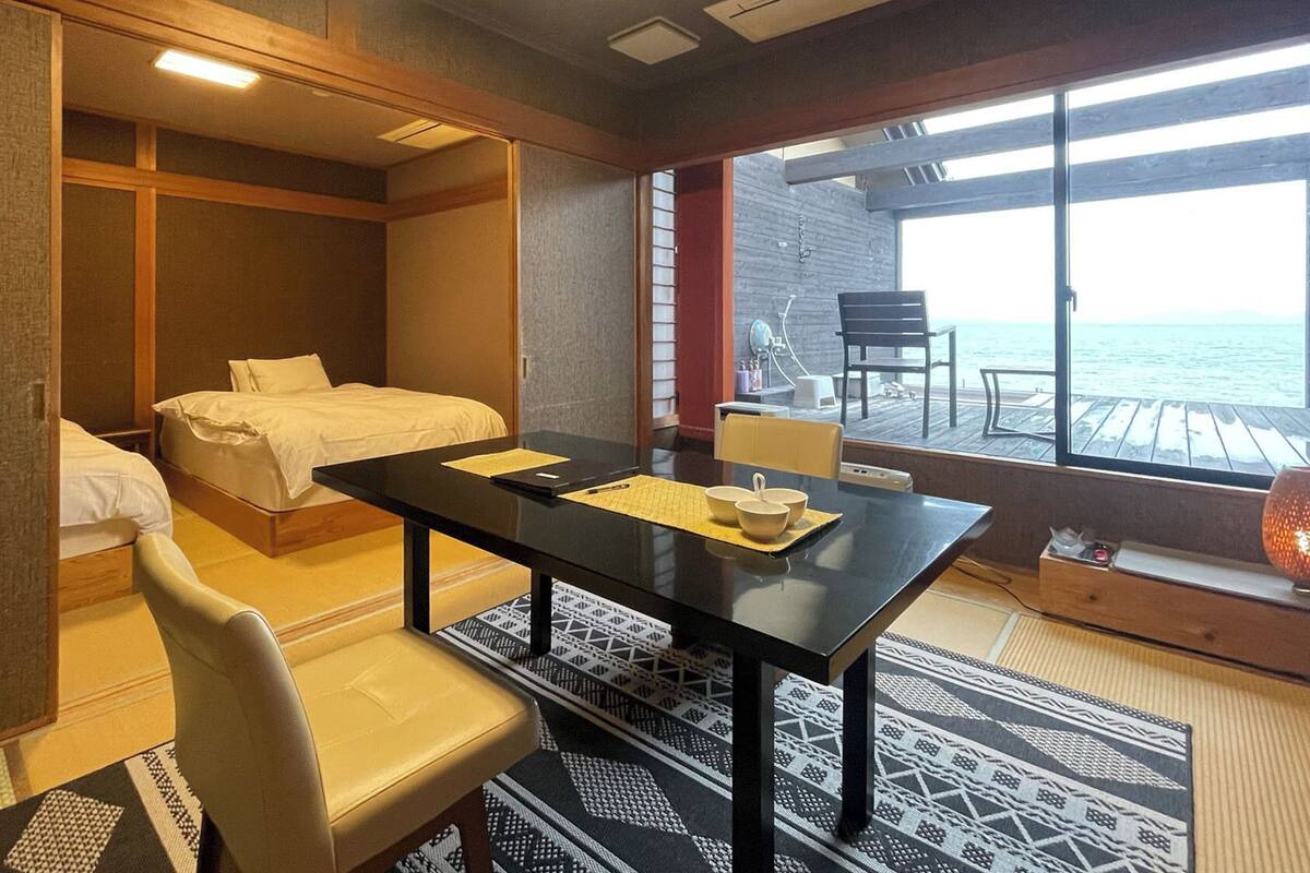 A hotel room with a bed, a desk, a chair, and a view of the sea.
