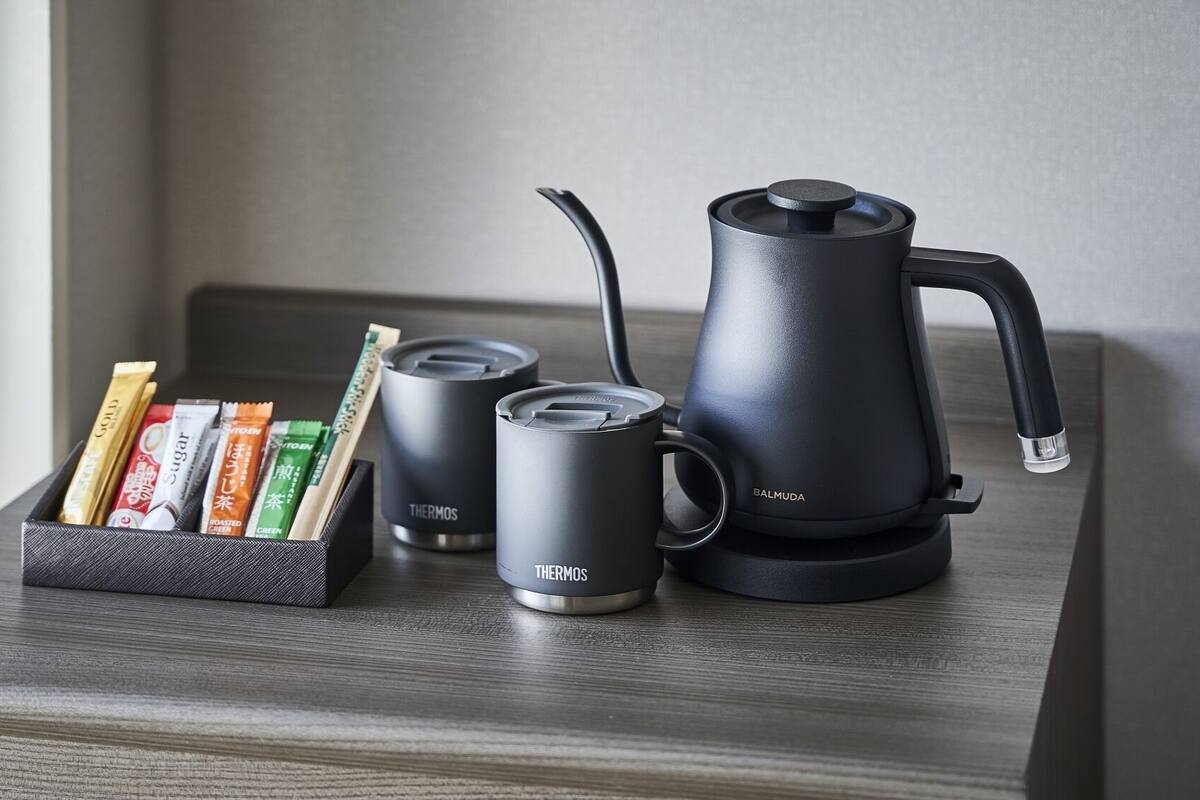 A black electric kettle, two black insulated mugs, and a box with tea bags on a wooden surface.
