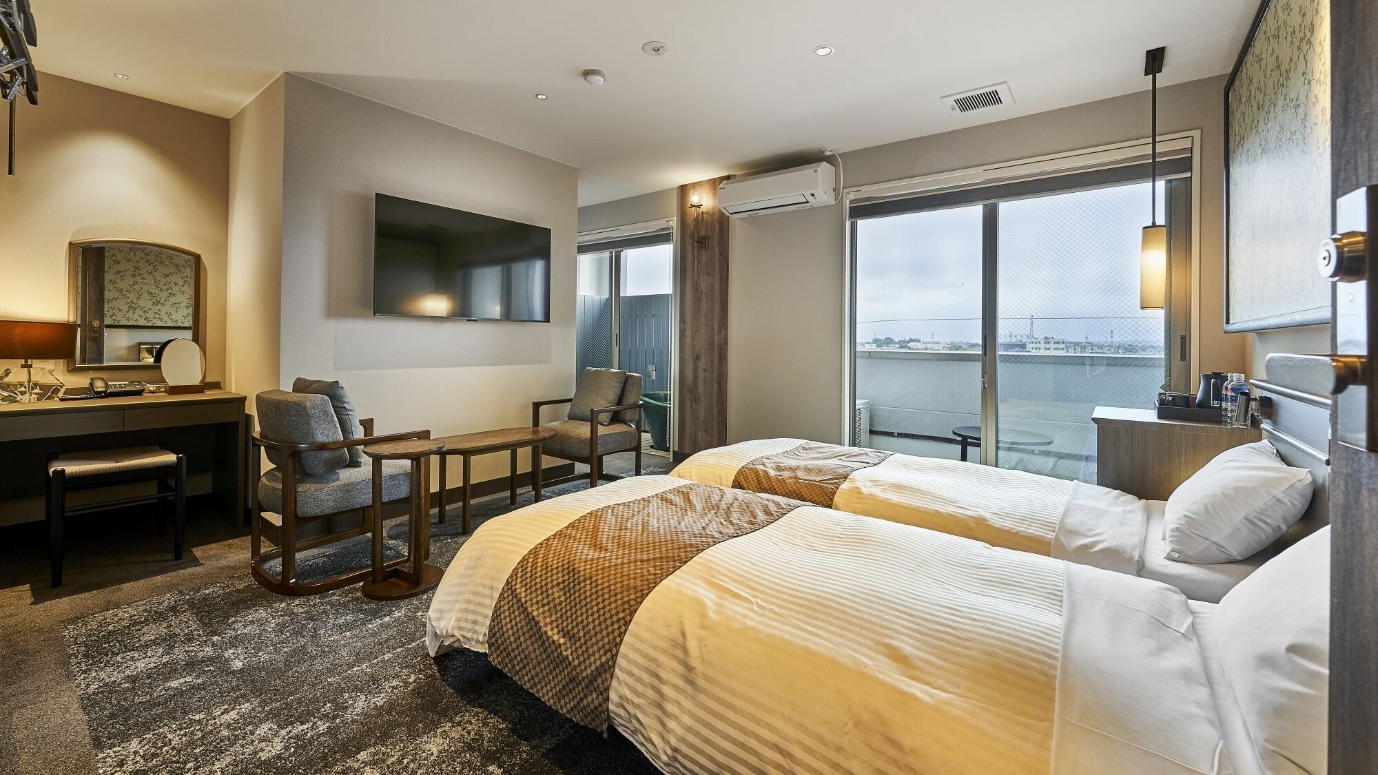 A hotel room with two beds, a desk, a chair, a TV, and a large window with a view.