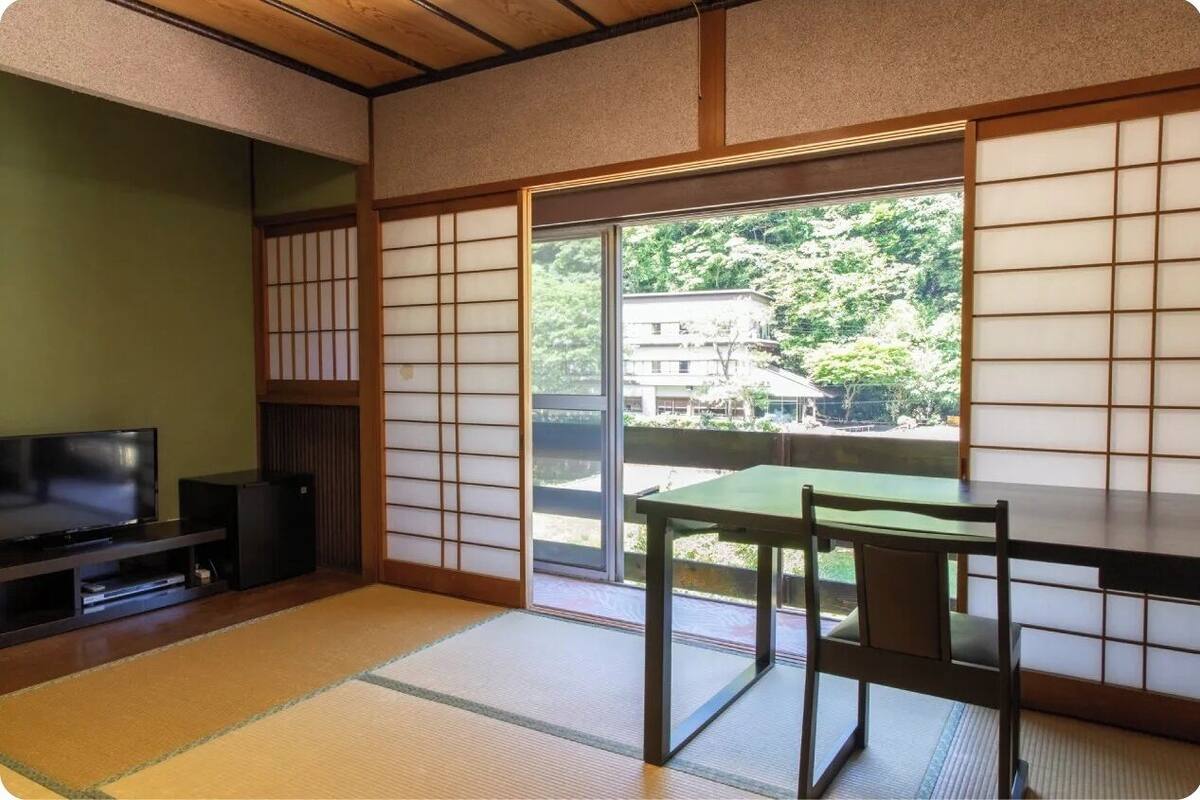 A traditional Japanese room with tatami flooring, a sliding door, a television, and a table with a chair.