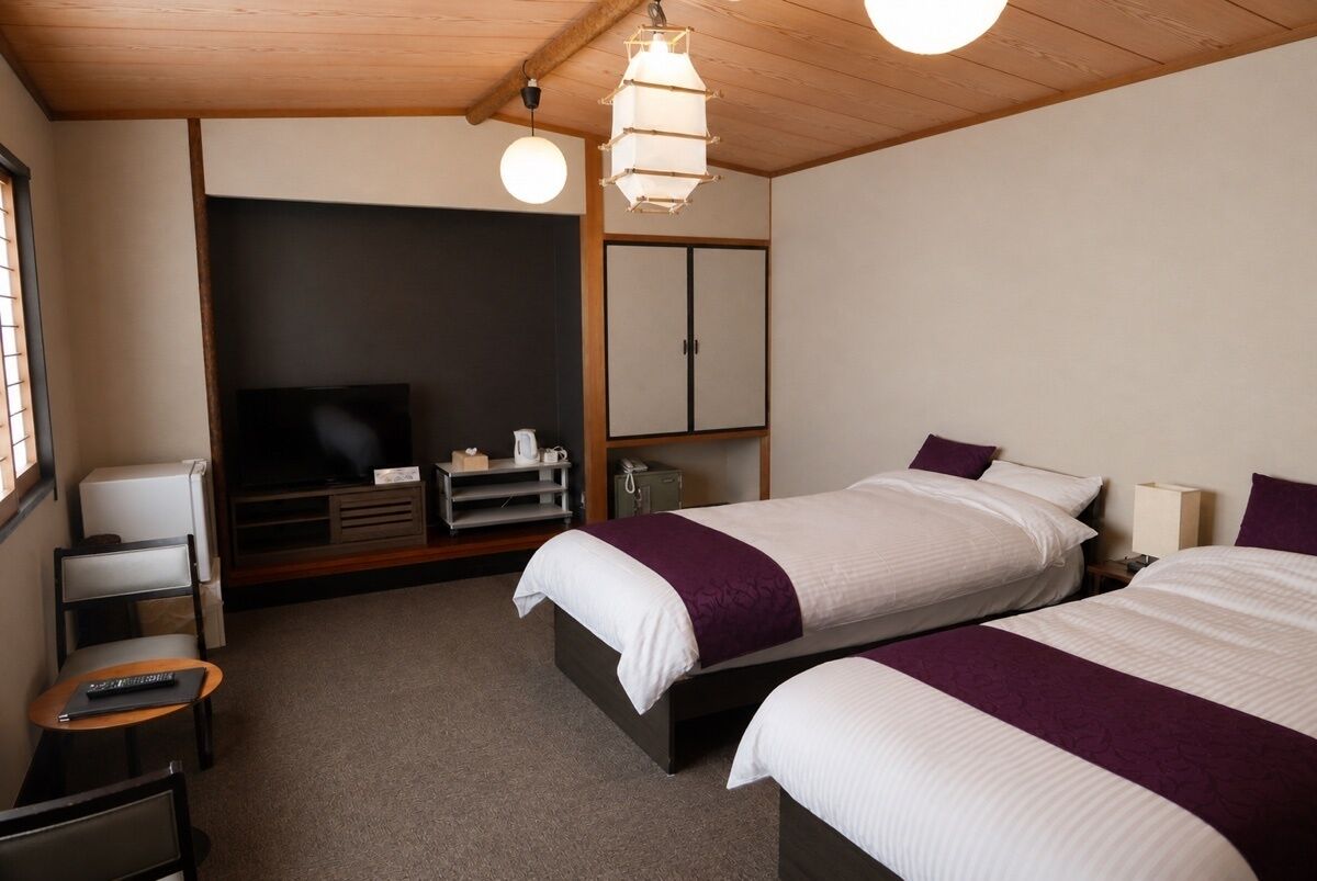 Ein Hotelzimmer mit zwei Betten, einem Fernseher, einem Schreibtisch und einem Kleiderschrank.