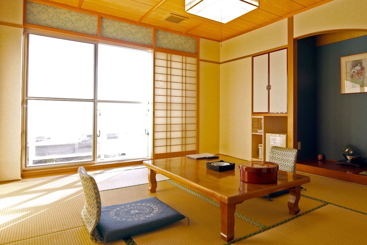 A traditional Japanese room with tatami flooring, a low table, a chair, sliding doors, and a dark wall with a framed picture.