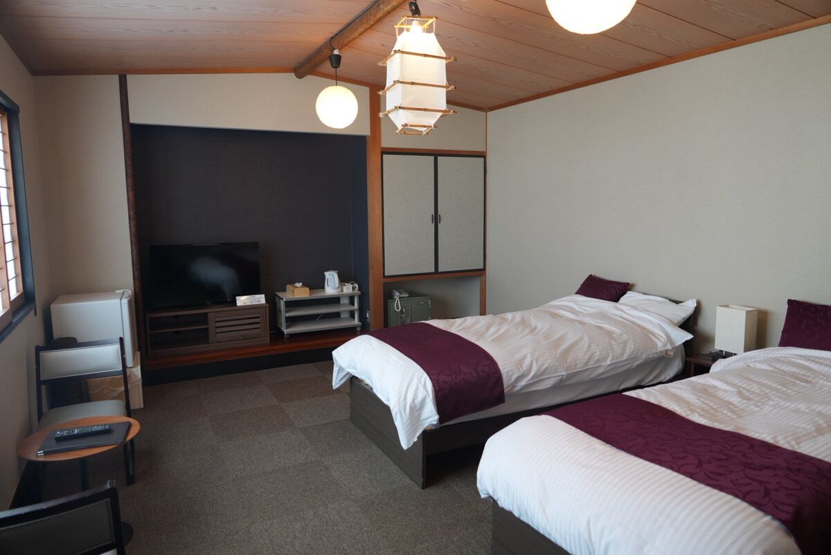 Ein Hotelzimmer mit zwei Betten, einem Fernseher, einem Kleiderschrank und einem Schreibtisch mit Stuhl.