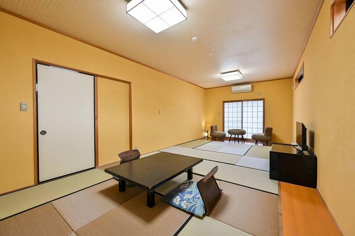 A tatami mat room with a sliding door, a table, chairs, and a television.