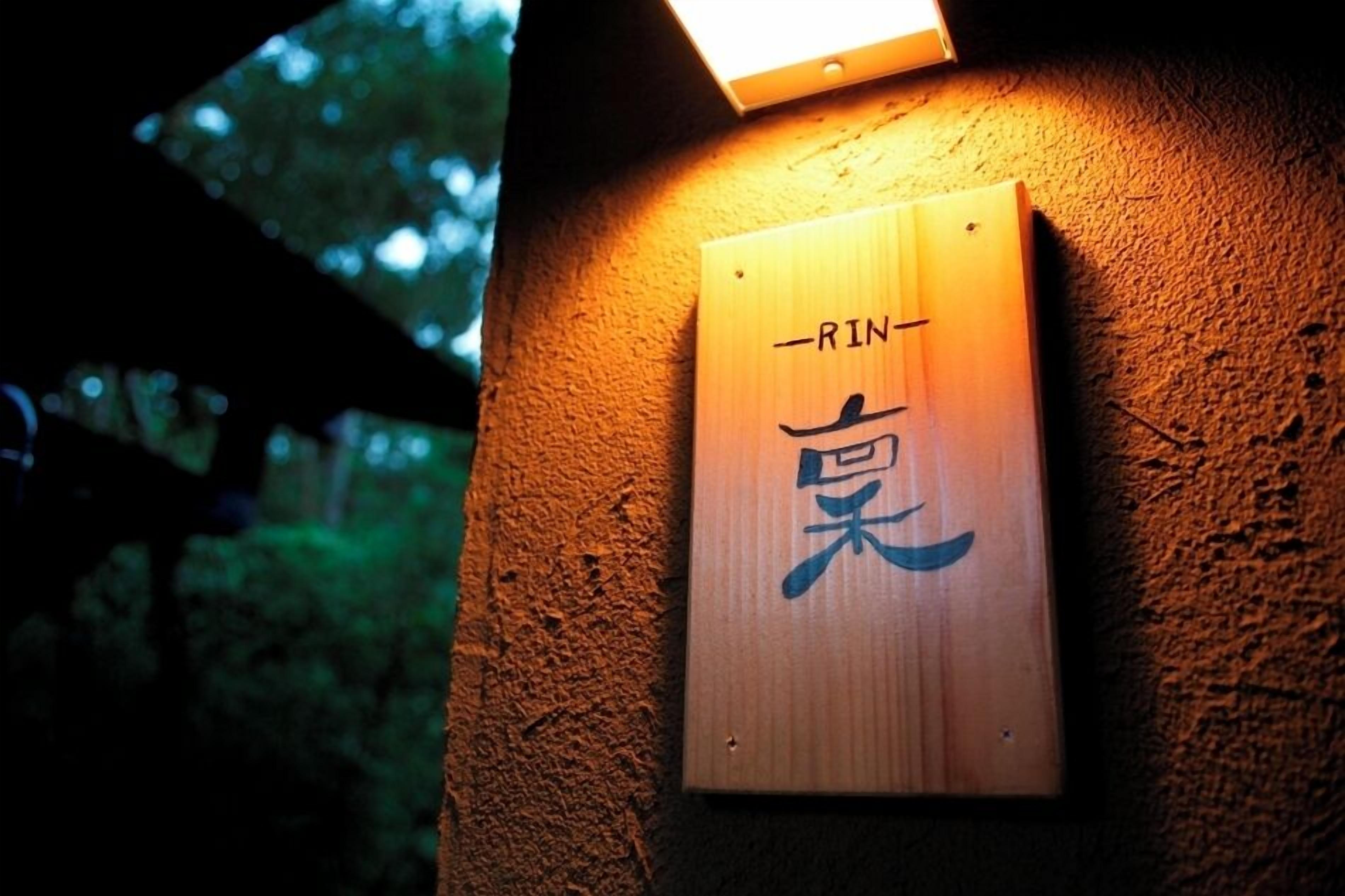 Un letrero de madera con caracteres japoneses, sujeto a una pared con textura, iluminado por una lámpara.