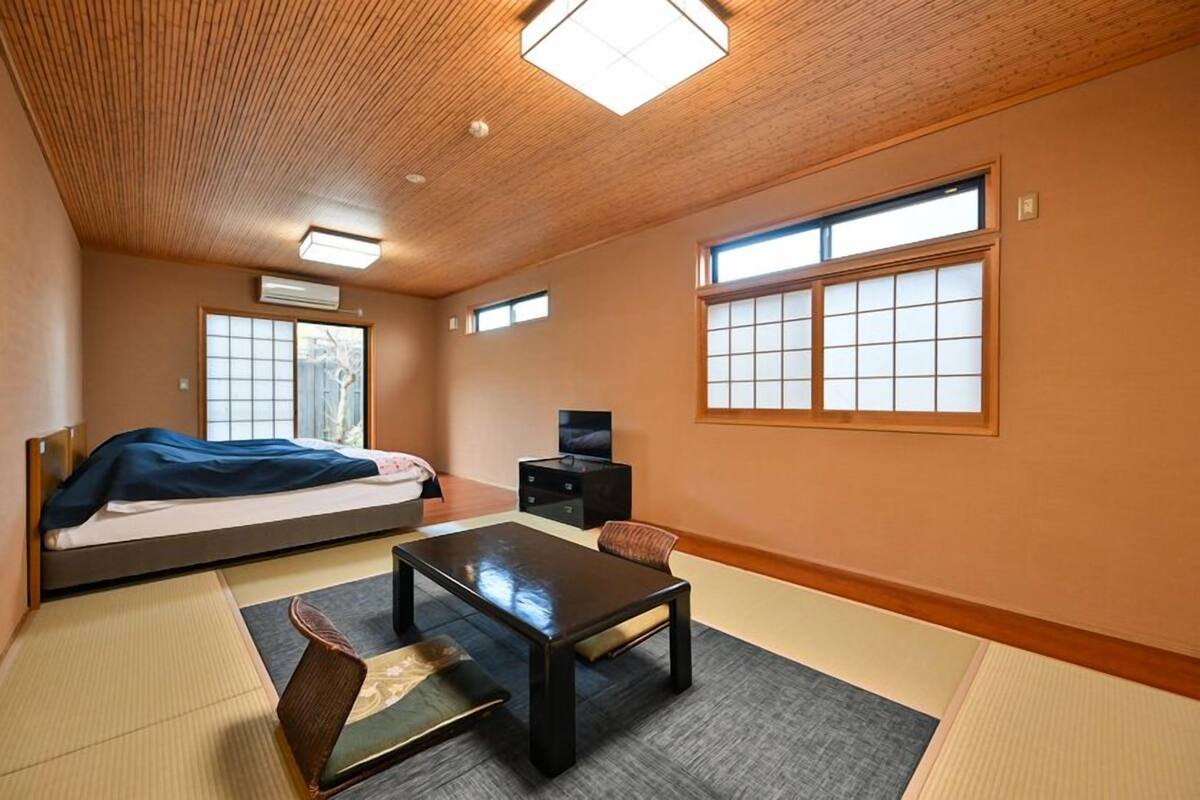 A room with tatami flooring, a bed, a table, and a TV.