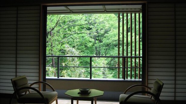 A room with tatami flooring, a low table with a bowl, two chairs, and a large window with vertical blinds. - Worifushi no Yado Shougetsu (Koriyama)