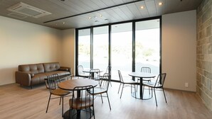 A modern interior with a sofa, round tables, and chairs, large windows, and a stone wall. - Ties Verde Hotel (Okuma)