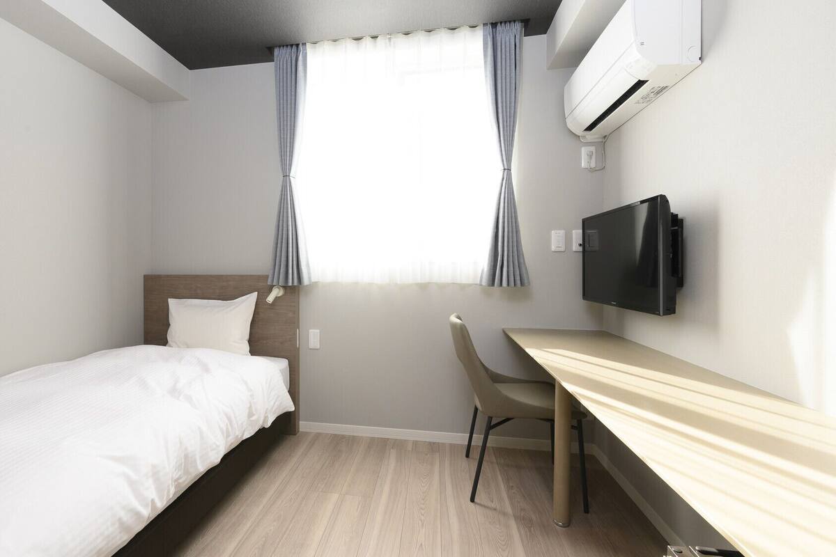 Una habitación de hotel con cama, escritorio, silla, televisor y aire acondicionado.