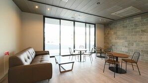 A modern interior with a sofa, tables, chairs, large windows, and a stone wall. - Ties Verde Hotel (Okuma)