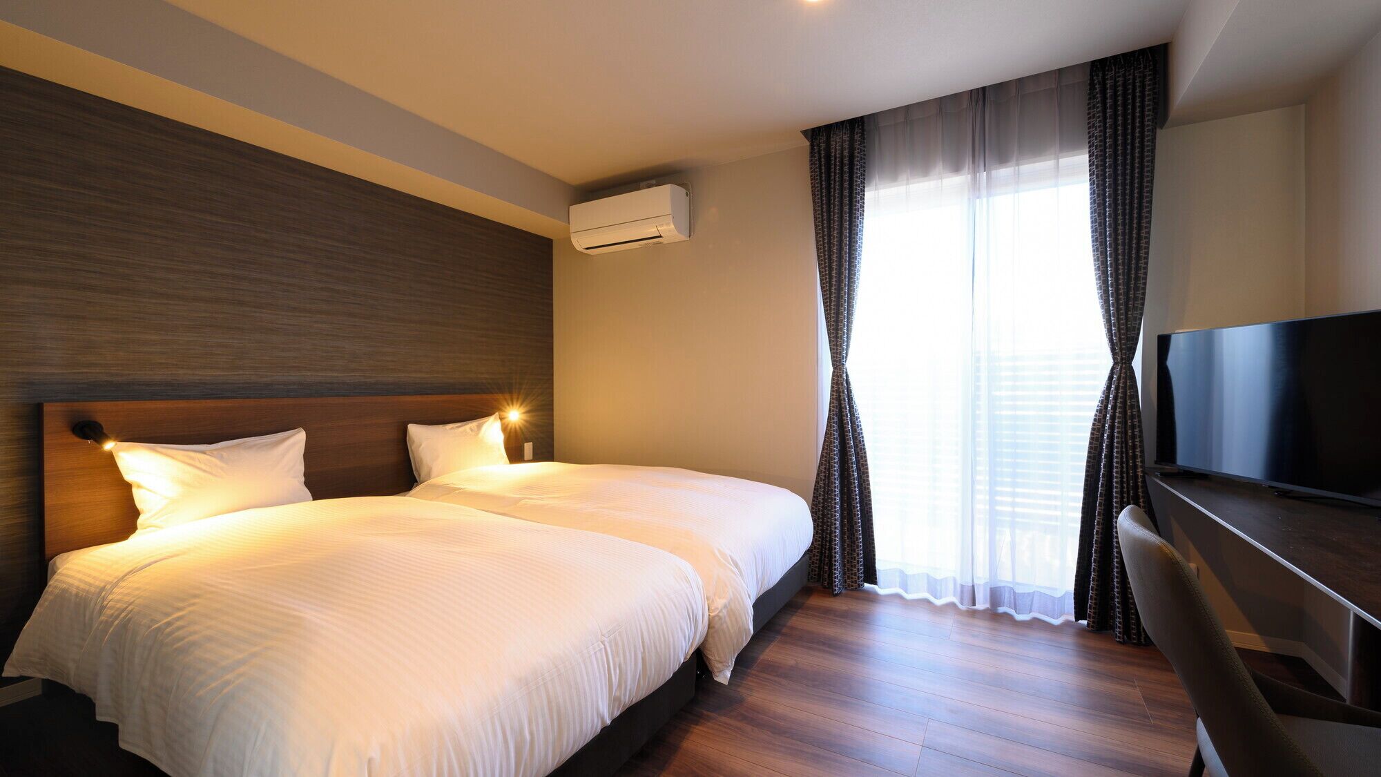 A hotel room with two beds, a TV, and an air conditioning unit.