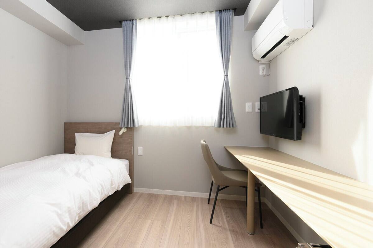 Habitación de hotel con cama, escritorio, silla, televisor y aire acondicionado.